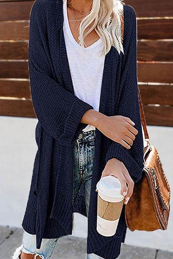 Navy open-front cardigan worn with the sleeves extending past the wrists and the long hem framing jeans.