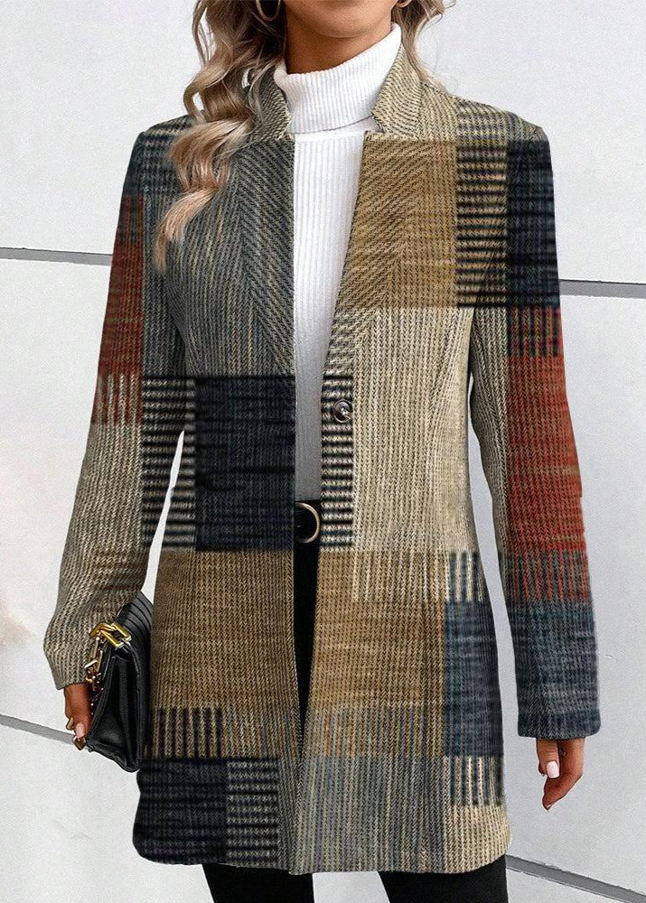 Long patchwork plaid blazer shown from the front against a light wall, highlighting its varied rectangular checks, extended hem, notched lapels, and long sleeves.