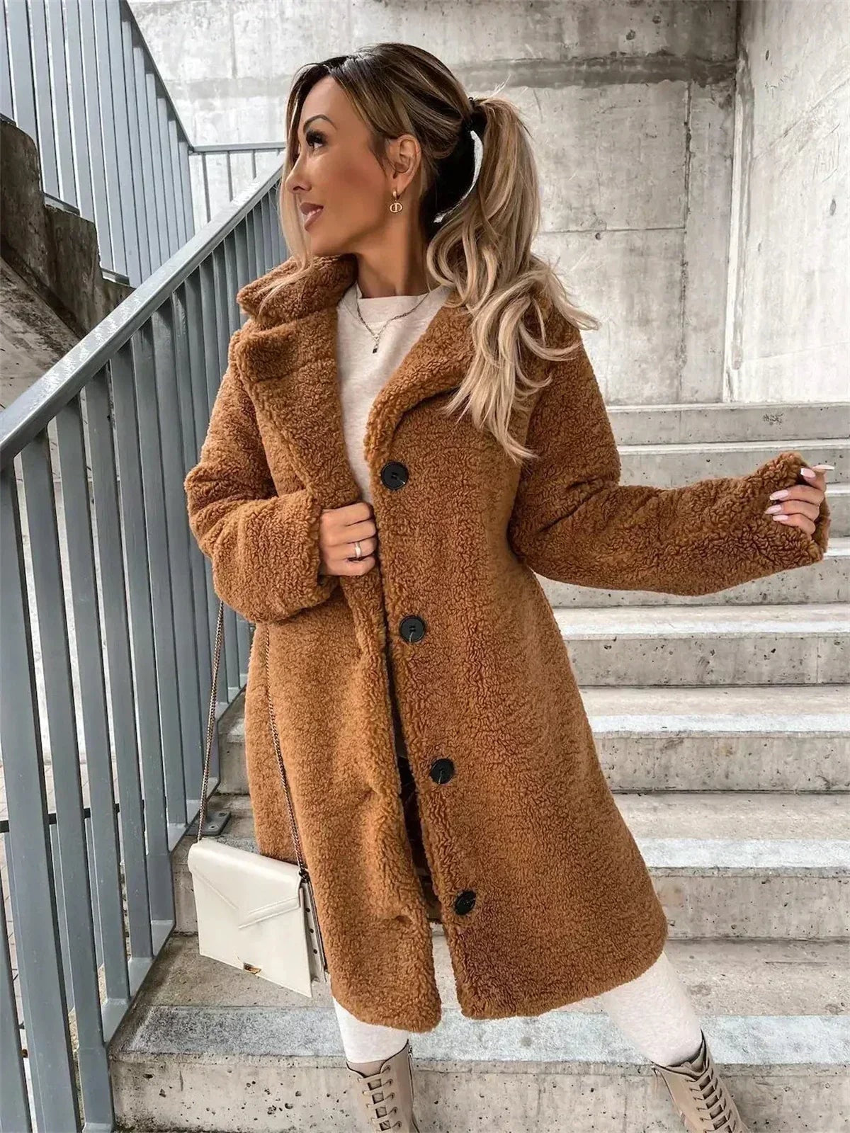 Front three-quarter view of the tan teddy coat with one sleeve extended, highlighting the textured finish, notched collar, and aligned dark buttons.