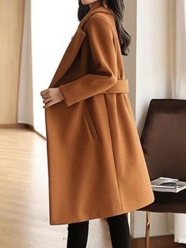 Side view of a camel-colored long trench coat showing its below-knee length, belted waist tab, long sleeve, and angled front pocket.
