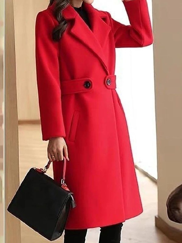 Bright red long trench coat with wide lapels, two-button waist tab, long sleeves, and angled front pockets, paired with black trousers.