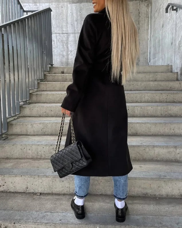Rear three-quarter view of a black longline coat showing its extended length, long sleeves, and clean back silhouette.