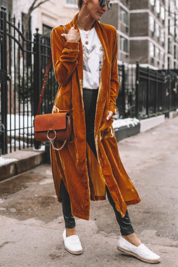 Outdoor three-quarter view of the mustard open-front coat layered over a graphic top and black trousers.