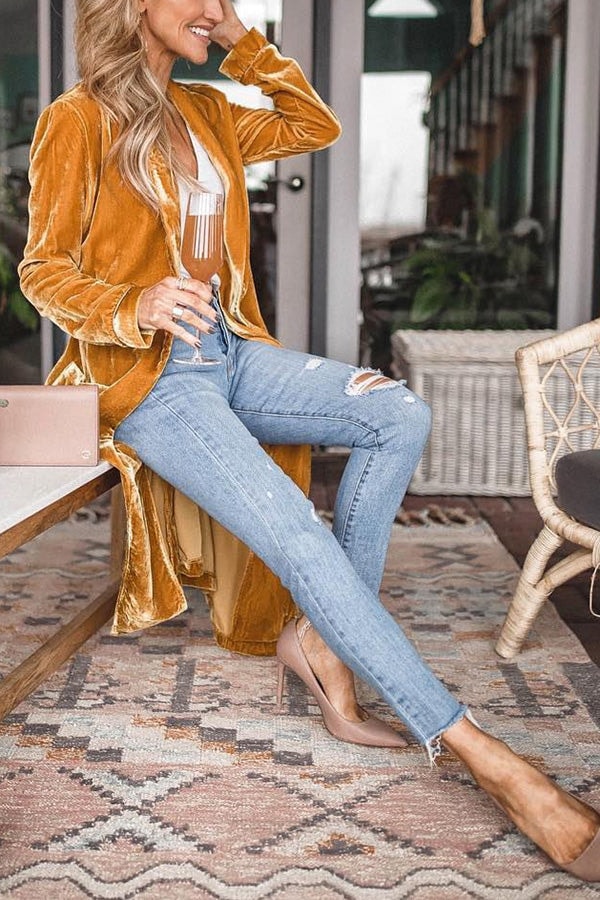 Mustard open-front coat draped behind a seated model, with the sleeve ruching visible in profile.
