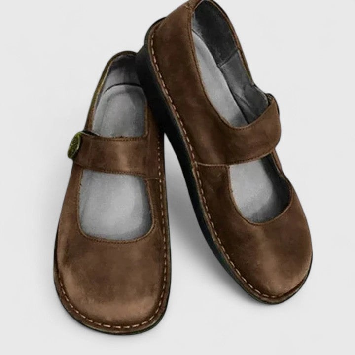 Brown Mary Jane flats arranged at an angle, clearly showing the front openings, instep straps, and contrast stitching along the soles.