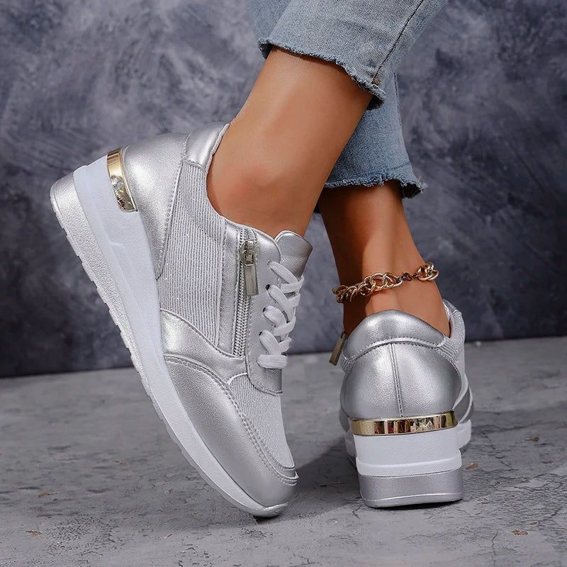 Silver metallic platform sneaker shown from the side with white laces, a side zip, and gold-toned heel accents.