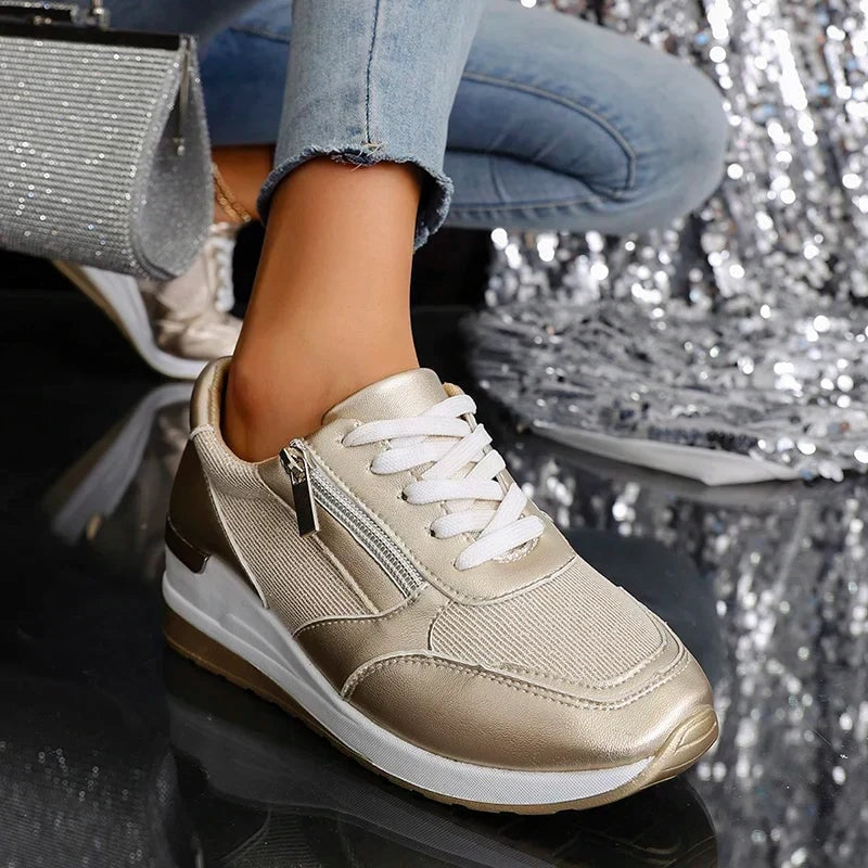Close view of one champagne metallic sneaker showing its textured side panel, white laces, side zip, and platform sole.