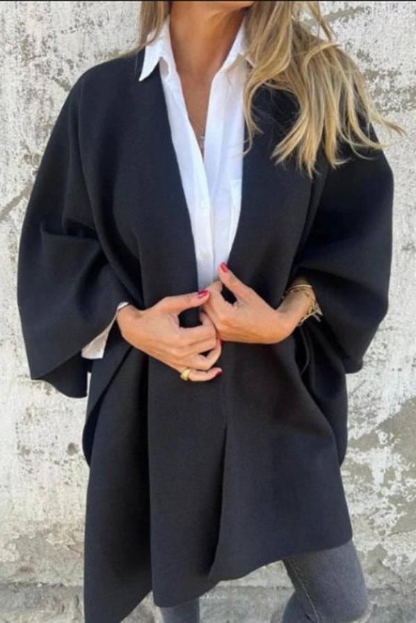 Black open-front cape jacket worn over a white collared shirt, with wide sleeves and an asymmetrical hip-covering hem.