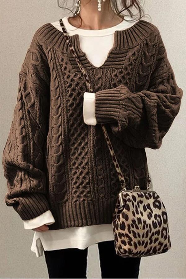 Brown oversized cable knit V-neck sweater with long sleeves and ribbed cuffs, layered over a white longline top.