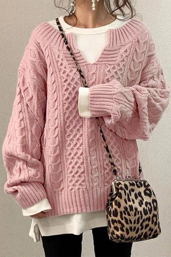 Pink oversized cable knit sweater with a V-neck, richly textured knit pattern, and long sleeves over a white underlayer.