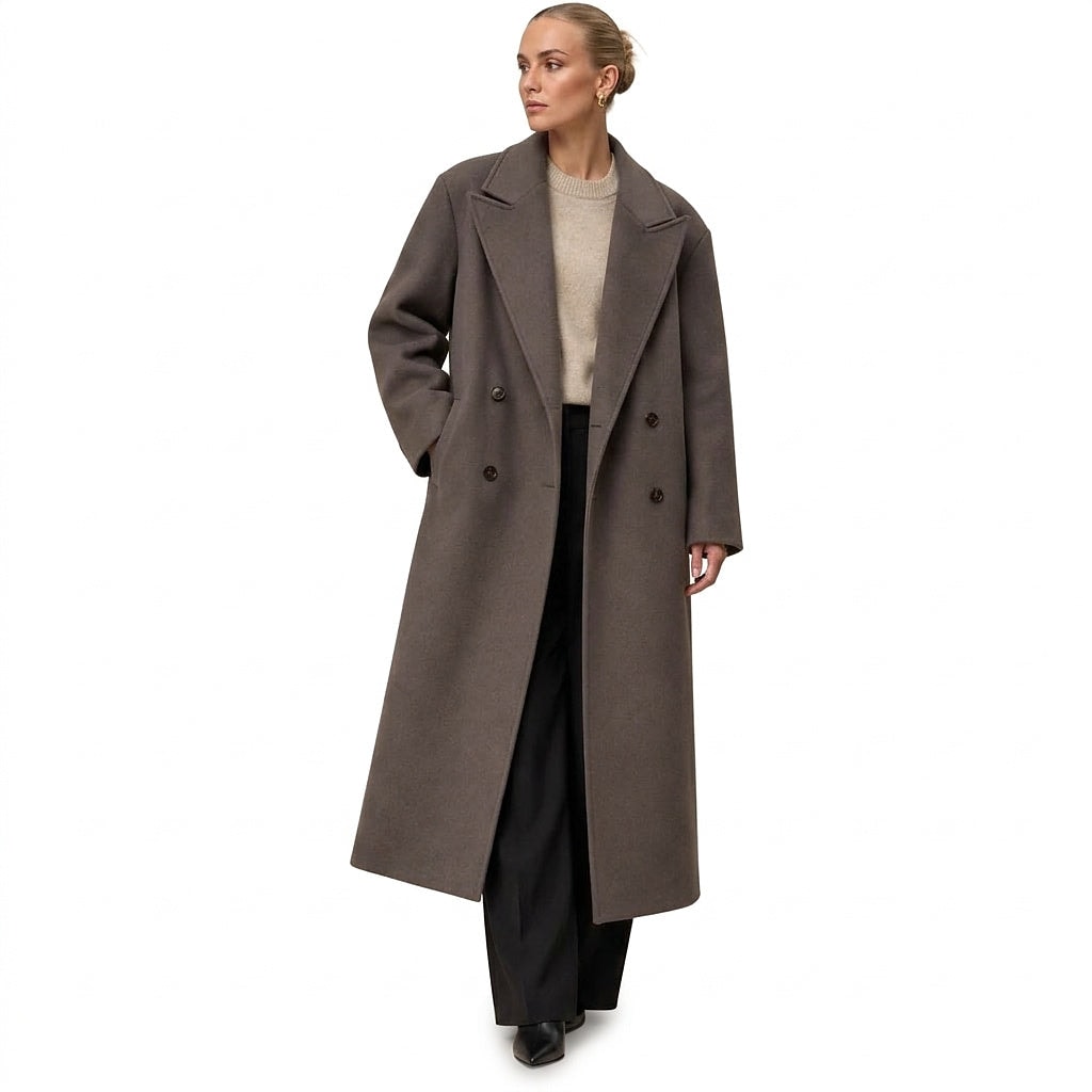 Front view of a taupe oversized long coat with wide lapels, double-breasted buttons, and side pockets, styled over a light sweater and black trousers.