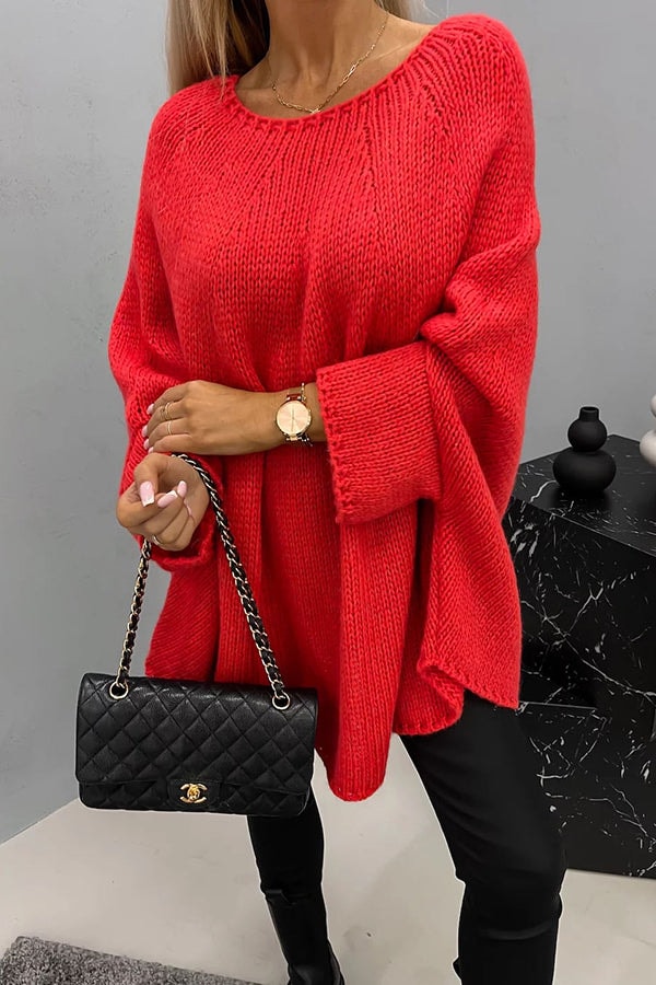 Bright red oversized knit poncho sweater with a crew neck, flowing wide sleeves, and curved hem worn with black trousers.