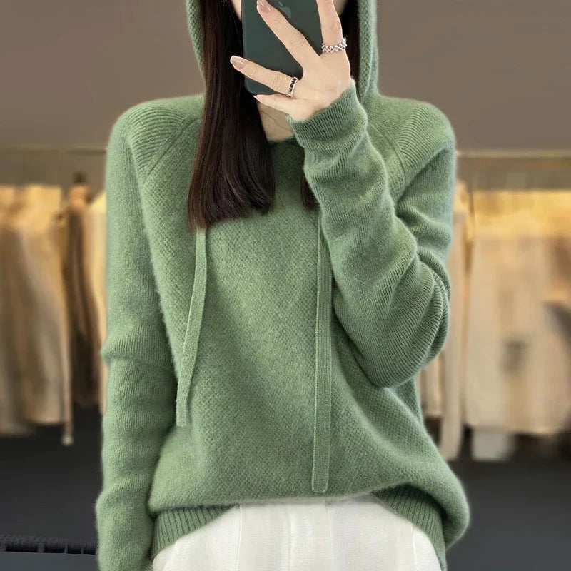 Sage-green oversized knit pullover hoodie shown with the hood raised, long drawstrings, and ribbed cuffs.