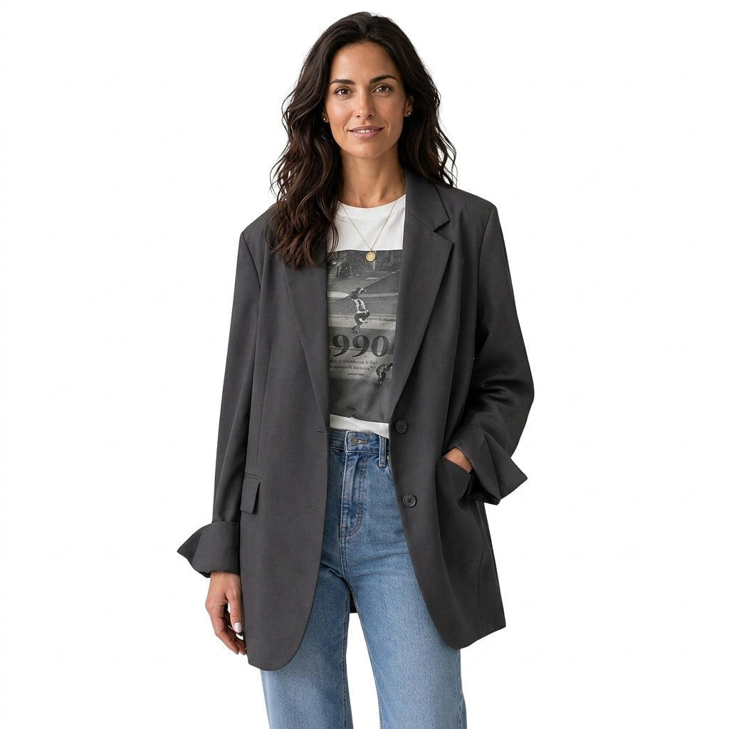 Front view of a charcoal oversized two-button blazer styled open over a graphic T-shirt and jeans, with notched lapels, flap pockets, and split cuffs.