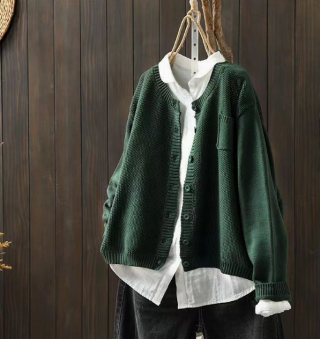 Dark green oversized V-neck cardigan layered over a white shirt, highlighting the button placket, ribbed cuffs, hem, and chest pocket.
