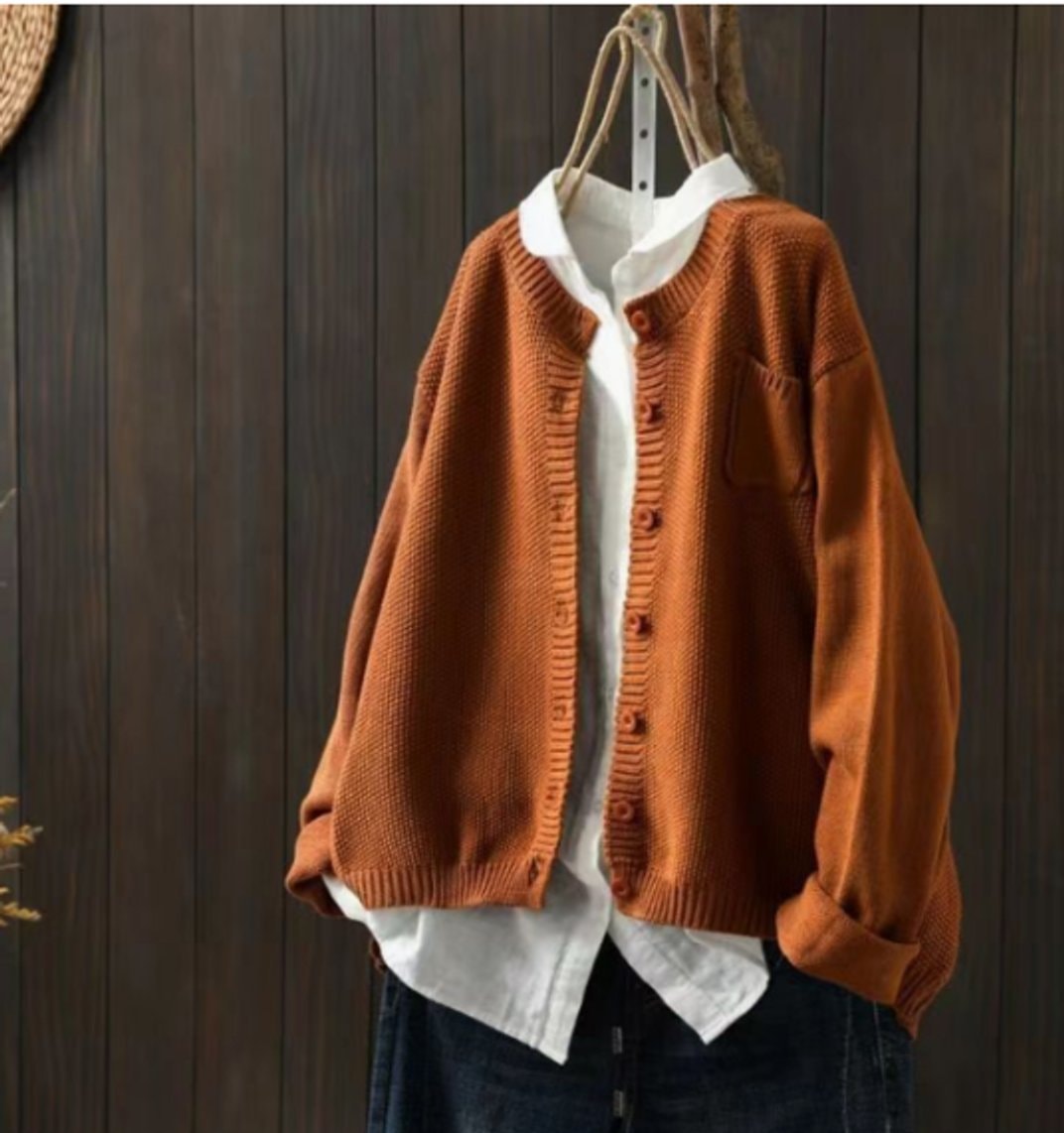 Rust-orange oversized cardigan worn open over a white shirt, with a visible patch chest pocket and gently rolled sleeve cuffs.
