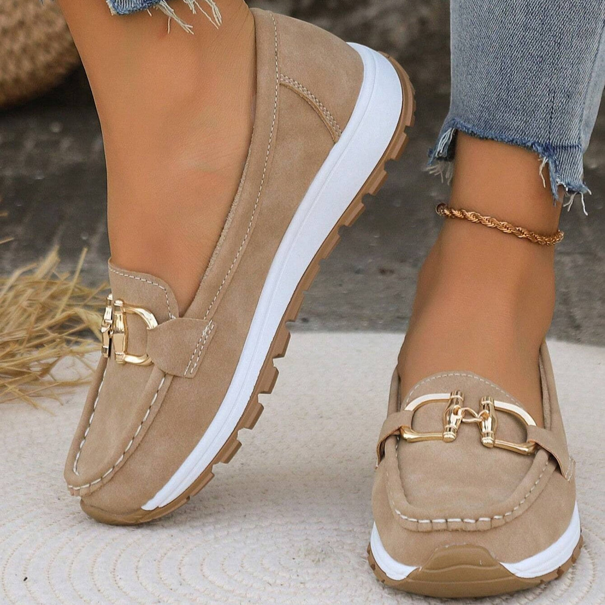 Beige platform loafers with rounded moc-toe stitching, gold-tone buckle details, white raised soles, and textured outsoles shown in a close-up view.