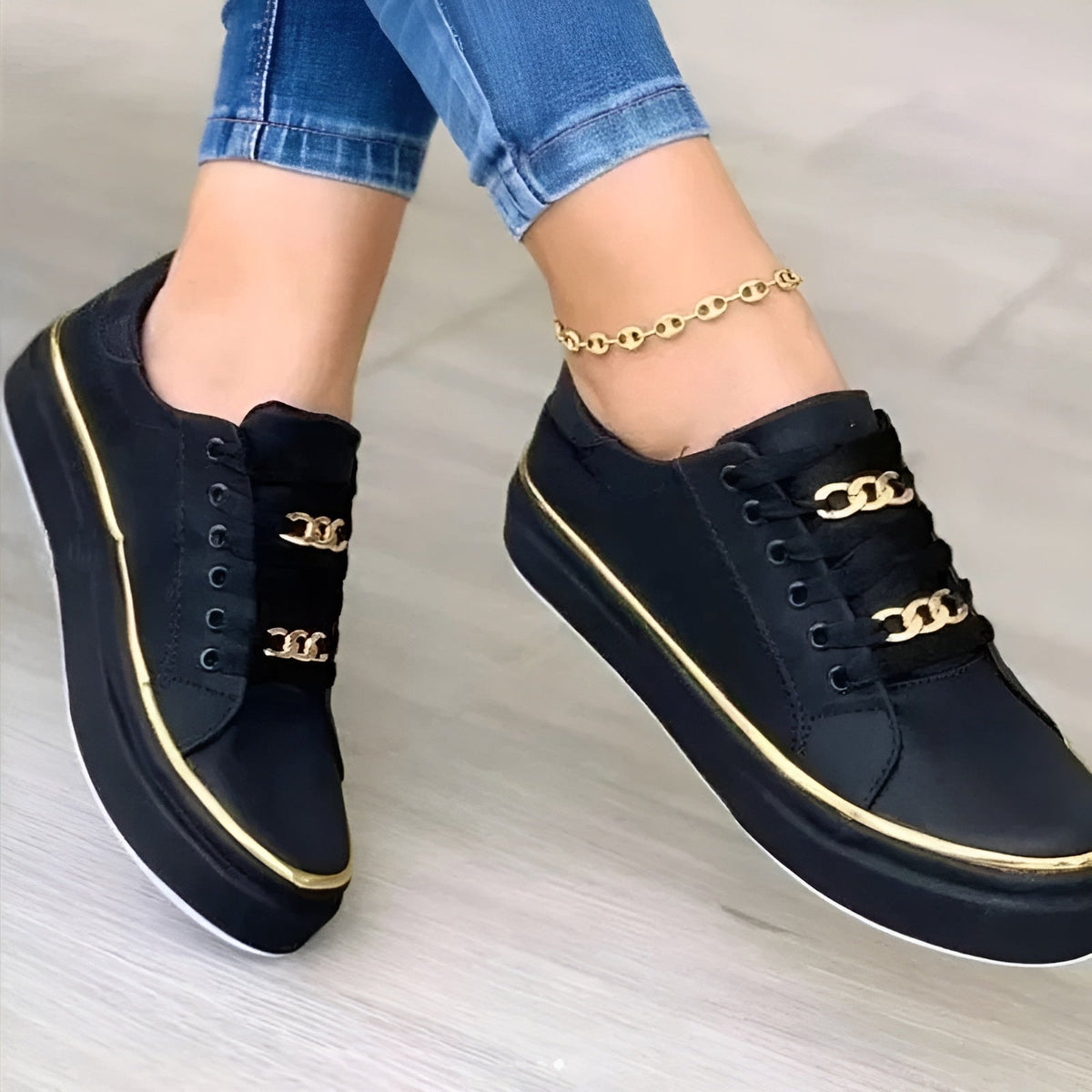 Close view of black low-top platform sneakers showing the lace-up eyelets, layered chain accents, rounded toes, and gold-tone side trim.