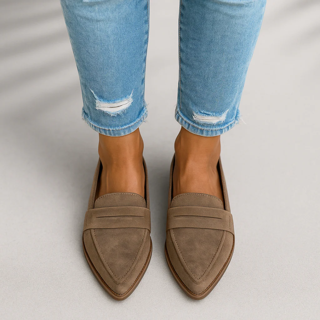 Taupe pointed toe slip-on loafers worn with light blue cropped jeans, shown from above with layered upper detailing.