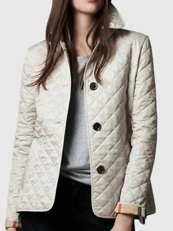 Light-colored quilted jacket styled over a gray top, featuring a pointed collar, dark buttons, and rolled checked cuffs.