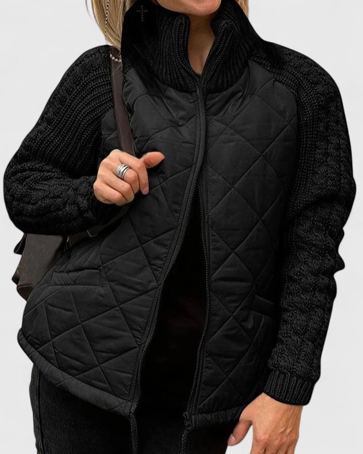 Black quilted jacket with matching textured long sleeves, raised collar, front zip, and angled side pockets.