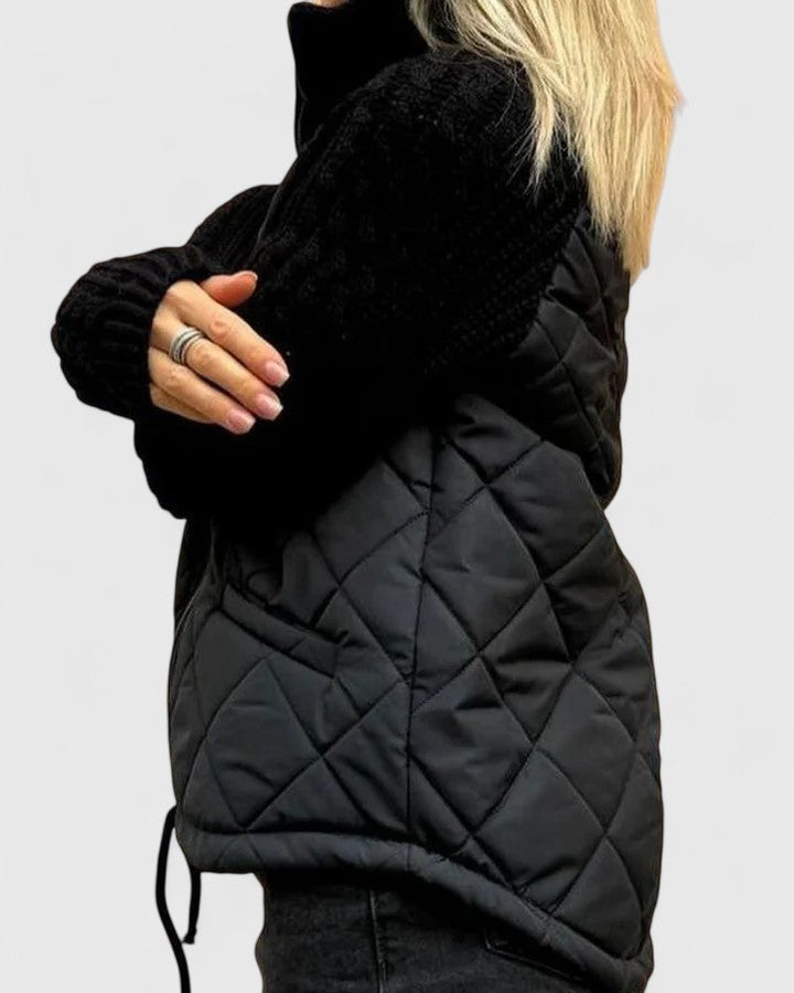 Side view of the black quilted jacket showing the textured sleeve, diamond quilting, raised collar, and adjustable drawcord hem.