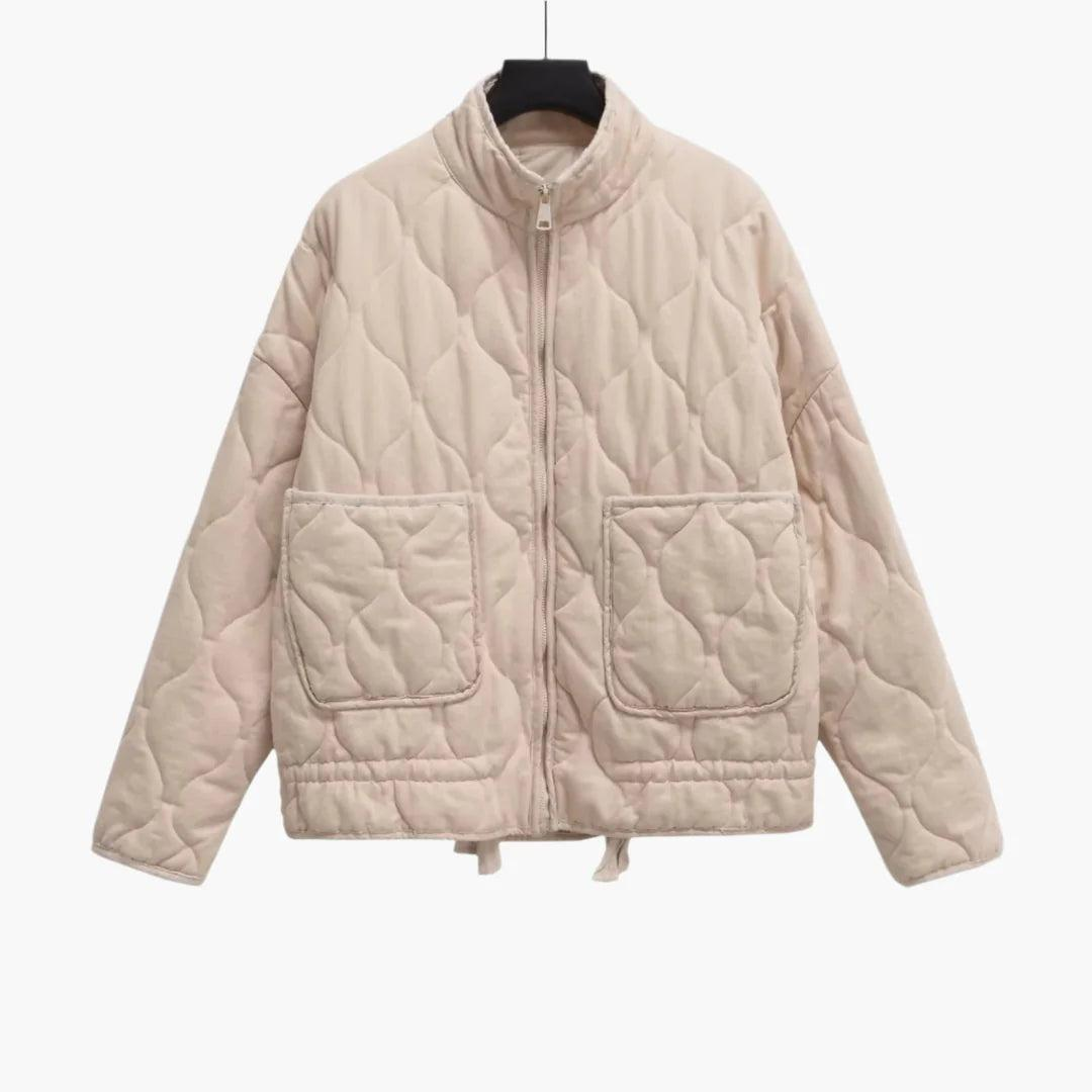 Front view of the short quilted jacket in a light cream shade, showing its raised collar, central zipper, long sleeves, and twin patch pockets.