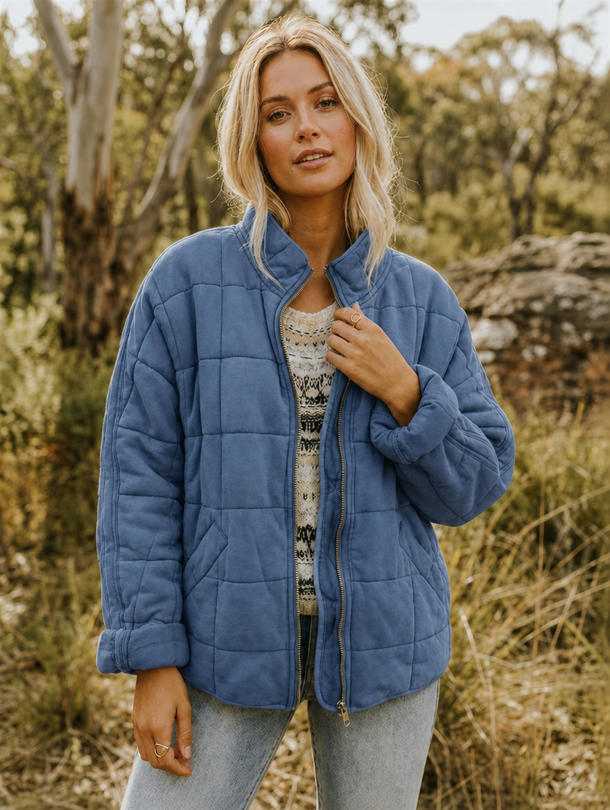 Front view of the jacket in blue, showing its stand collar, geometric quilting, zip closure, and patch pockets.