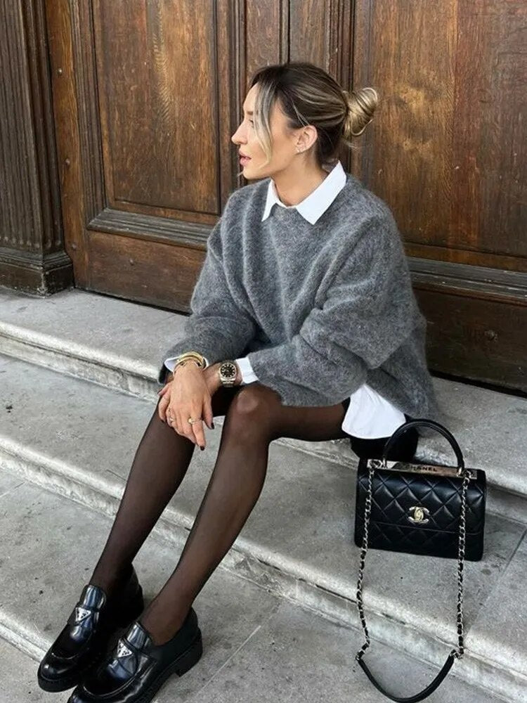 Gray relaxed crew-neck sweater layered over a white collared shirt, styled with a skirt and loafers.