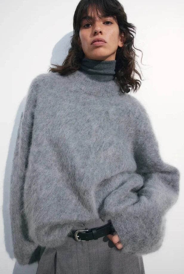 Gray relaxed sweater styled with tailored trousers, showing a loose silhouette and gathered long sleeves.