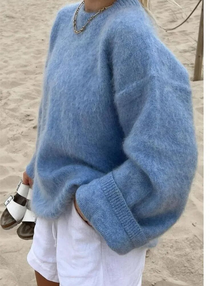 Side view of a blue relaxed sweater with an oversized sleeve and prominent turn-up cuff, styled with white shorts.