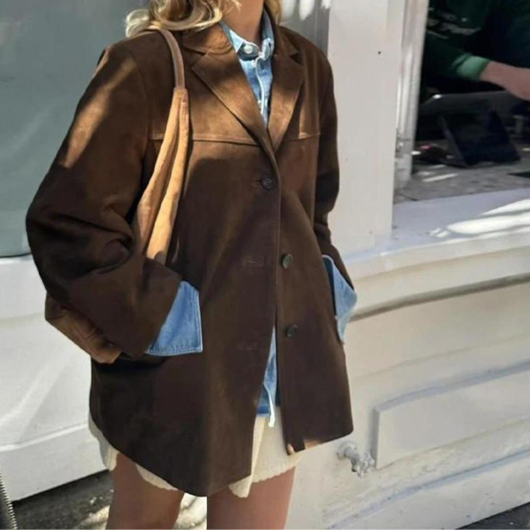 Brown blazer worn over a blue shirt and light shorts, showing the front fastening, notch lapels, roomy sleeves, and both lower front pockets.