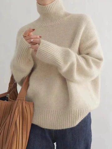 Cream turtleneck sweater displayed with its high ribbed neckline, relaxed body, long sleeves and blue jeans.