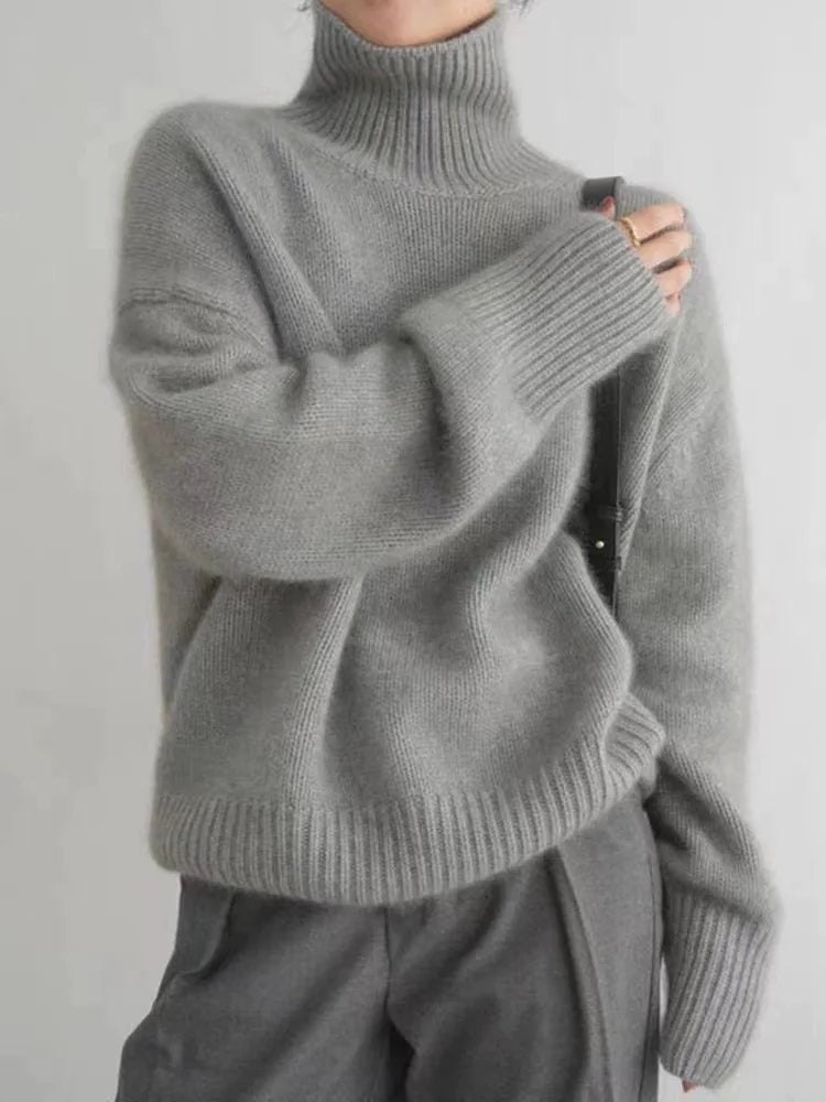 Gray relaxed turtleneck sweater featuring a high ribbed neck, long sleeves and a wide ribbed hem, styled with gray trousers.