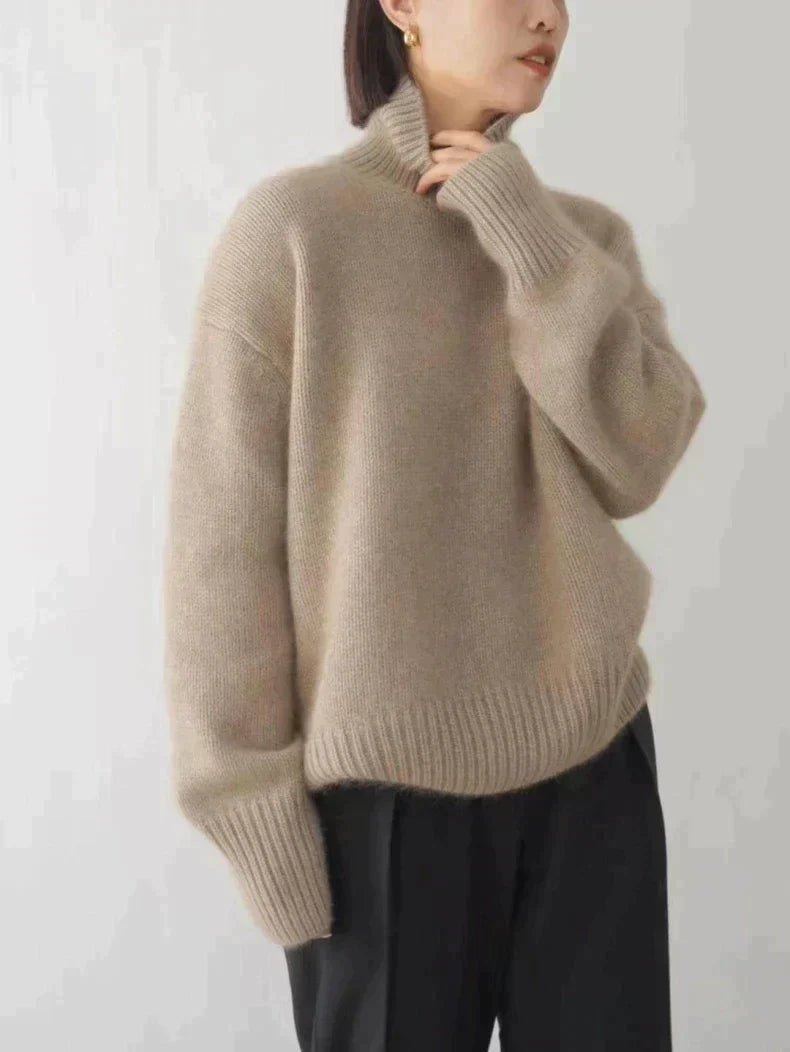 Beige turtleneck sweater shown in profile with a relaxed fit, long sleeve, ribbed cuff and hem, paired with black trousers.