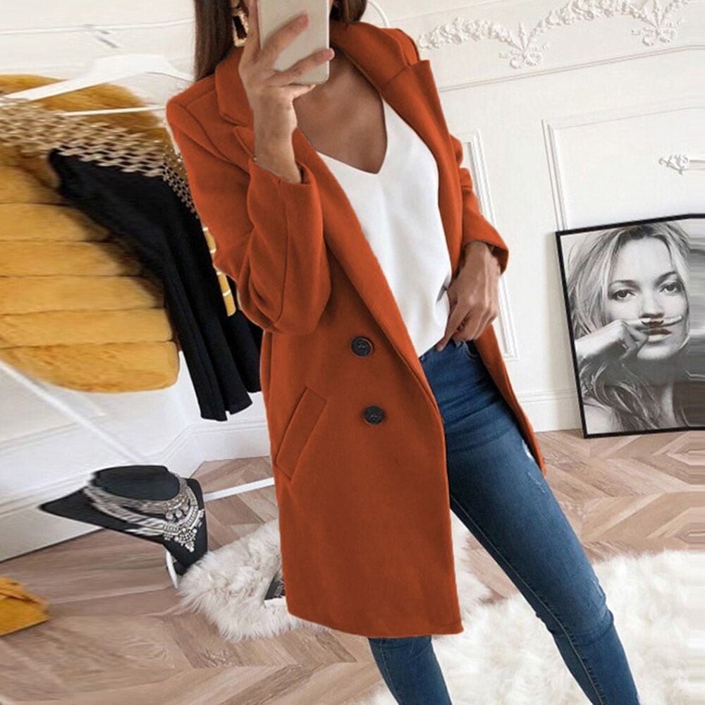 Rust-orange mid-thigh coat showing its structured notch lapels, two-button closure, and angled pockets over a white top and jeans.
