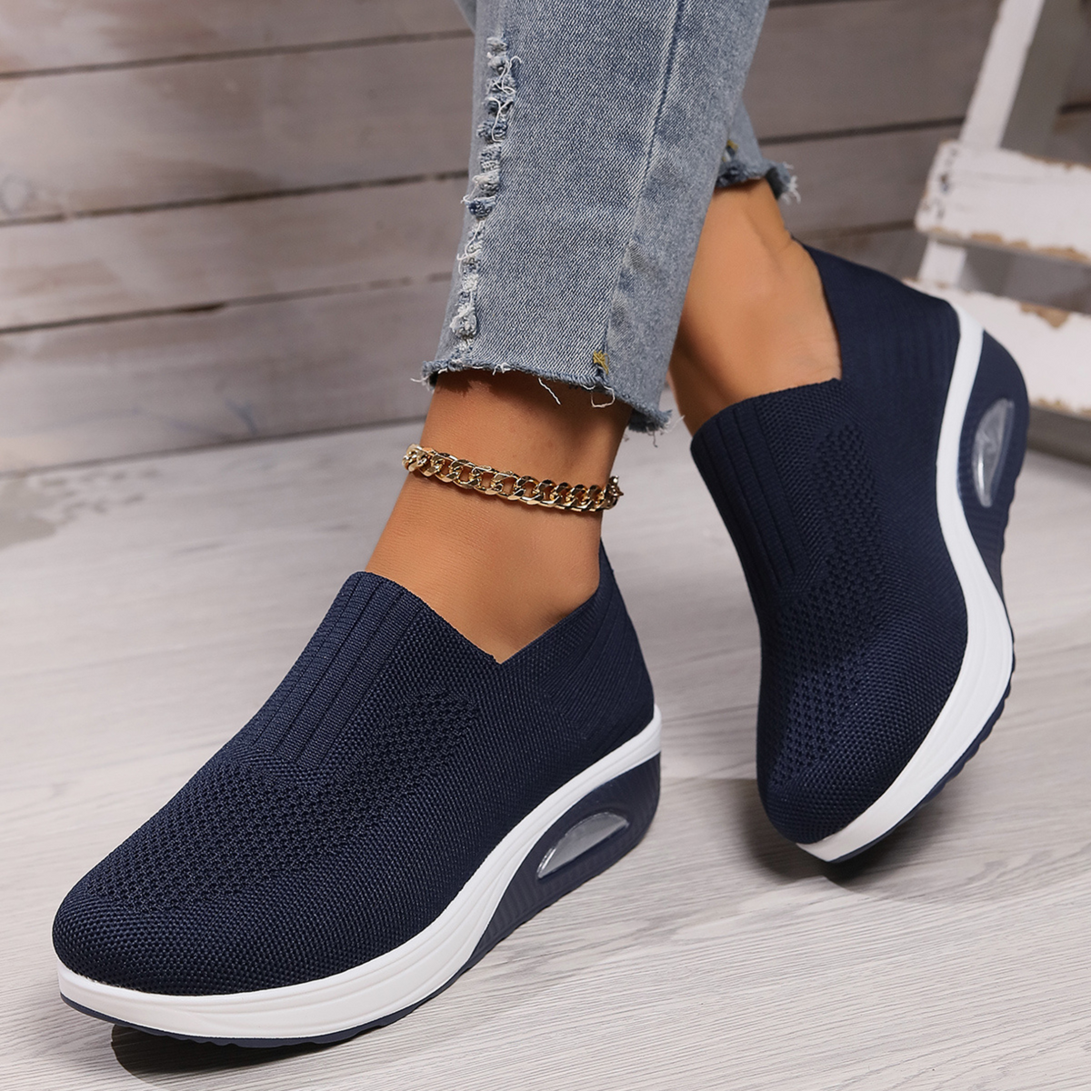 Navy slip-on platform sneakers worn from a three-quarter view, highlighting the contrasting white soles and textured low-cut uppers.