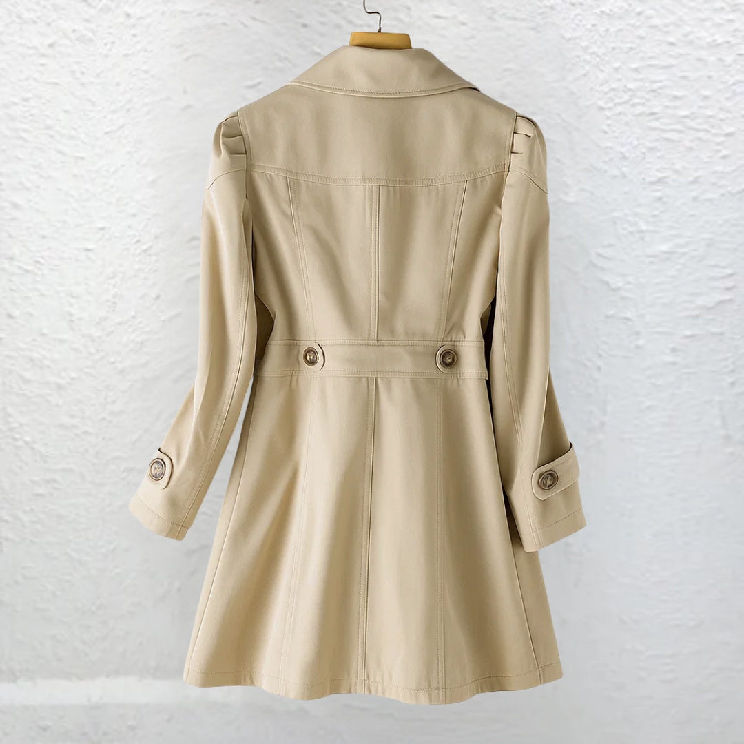 Rear view of a beige tailored trench coat showing the defined waist with button accents, structured back seams, long sleeves, and mid-thigh flared hem.