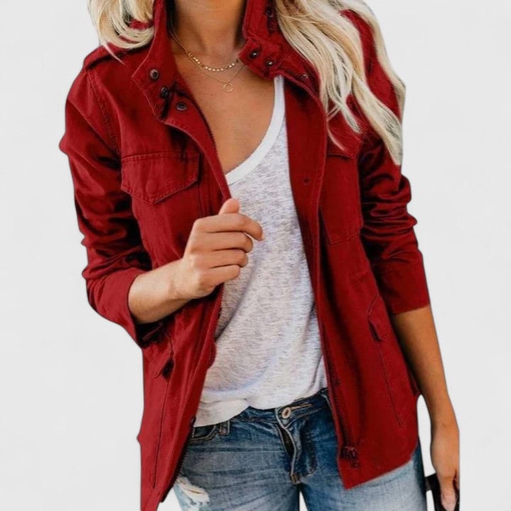 Red utility jacket worn open over a white top, with a high snap collar, flap chest pockets, long sleeves, and drawstring waist details.
