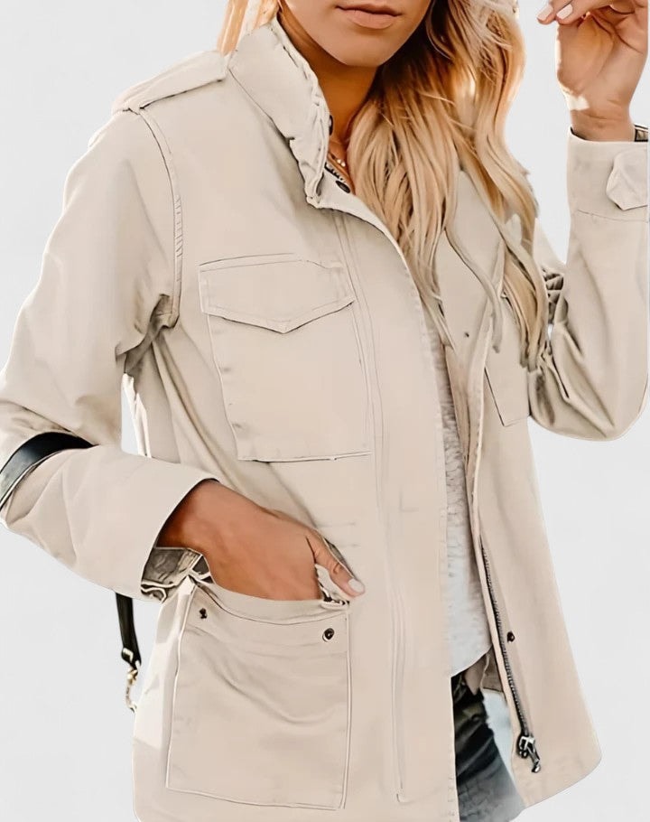 Front view of a light beige utility jacket with a raised collar, flap chest pockets, roomy lower pockets, and adjustable waist ties.