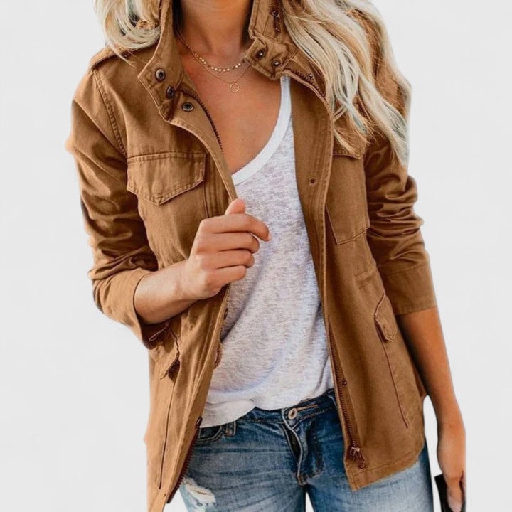 Brown utility jacket worn open over a white top, showing its high snap collar, flap chest pockets, hip-length shape, and waist drawstrings.