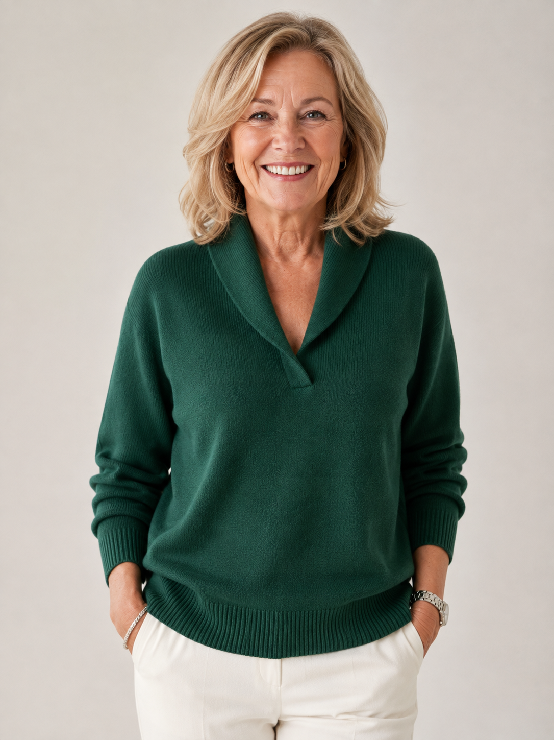 Dark green V-neck sweater with a shawl collar, long sleeves, and ribbed cuffs and hem, shown from the front with cream trousers.