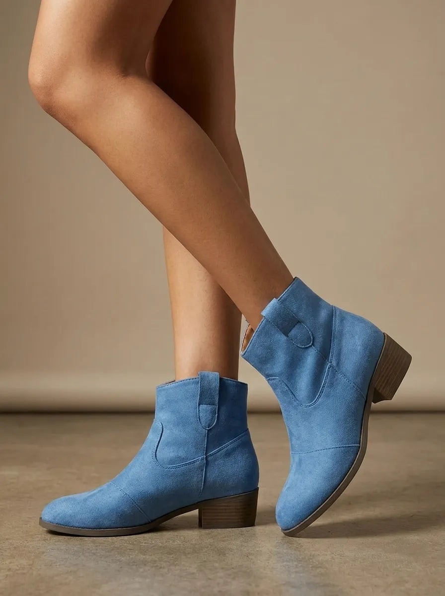 Blue Western ankle boots shown in motion from the side, highlighting the low block heels and decorative stitched panels.