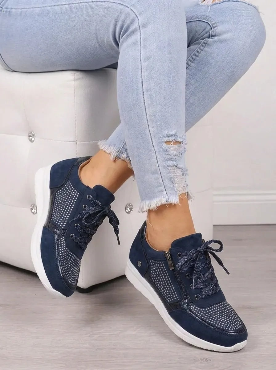Navy sneakers shown at an angled view while worn, highlighting the lace-up fronts, side zips, and textured white soles.
