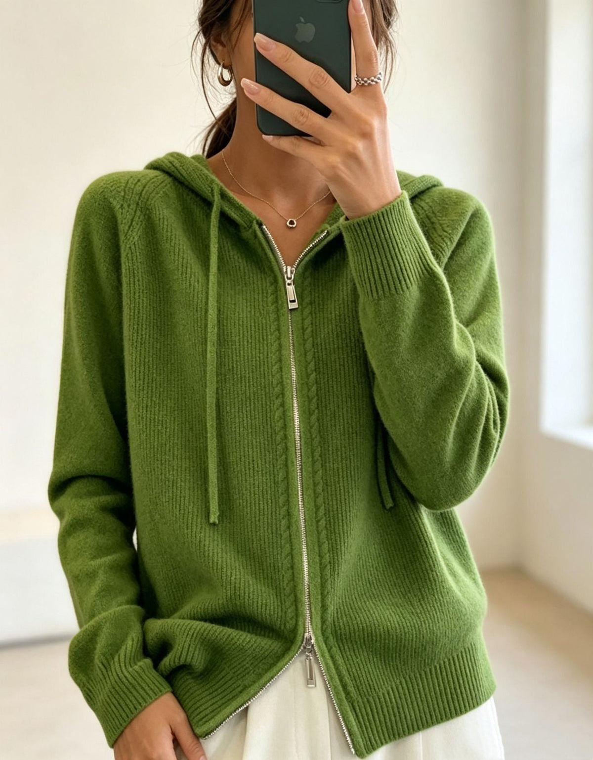 Olive green hooded cardigan worn zipped with long sleeves, hanging drawstrings and ribbed cuffs.