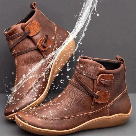 Brown ankle boots with adjustable wraparound side straps, rounded toes, contrast stitching, rear pull tabs, and low-profile soles shown with a water splash.