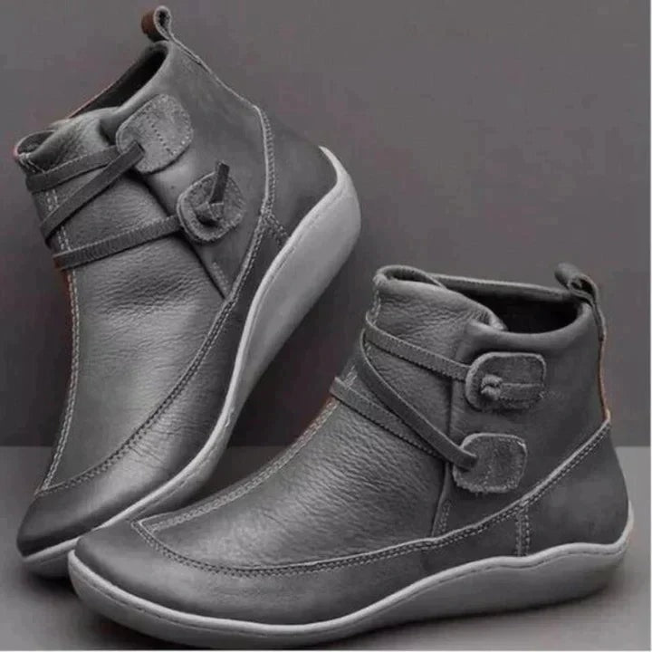 Gray ankle boots in a side-by-side angled arrangement, showing their rounded toes, layered side straps, contrast stitching, and practical ankle-height design.