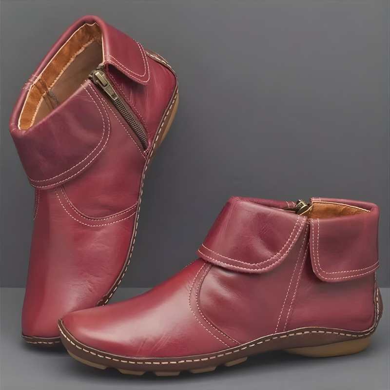 Burgundy ankle boots with layered wrap panels, contrast stitching, visible side zips, and textured flat soles shown from the side.