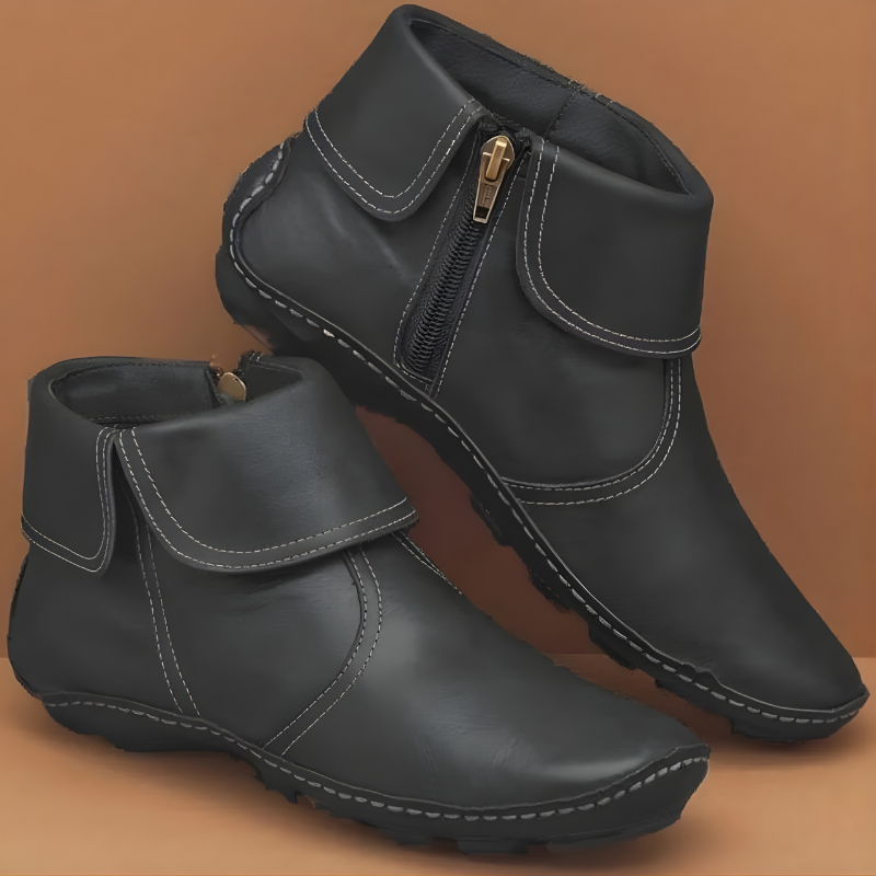 Black ankle boots shown in a paired angled view, with wrap panels, contrasting stitching, side zips, and rugged flat soles.