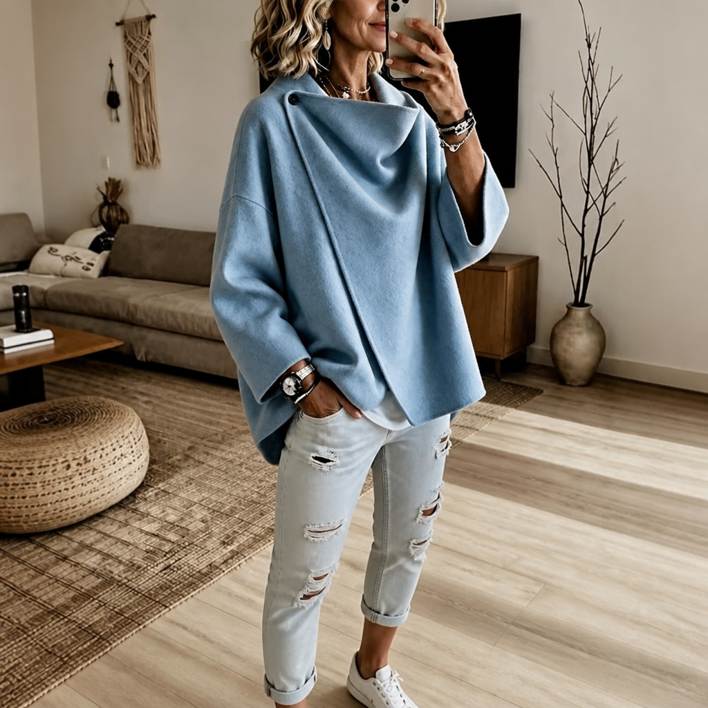 Light blue version of the asymmetric button wrap cape jacket with a draped collar and wide sleeves, styled with white jeans.